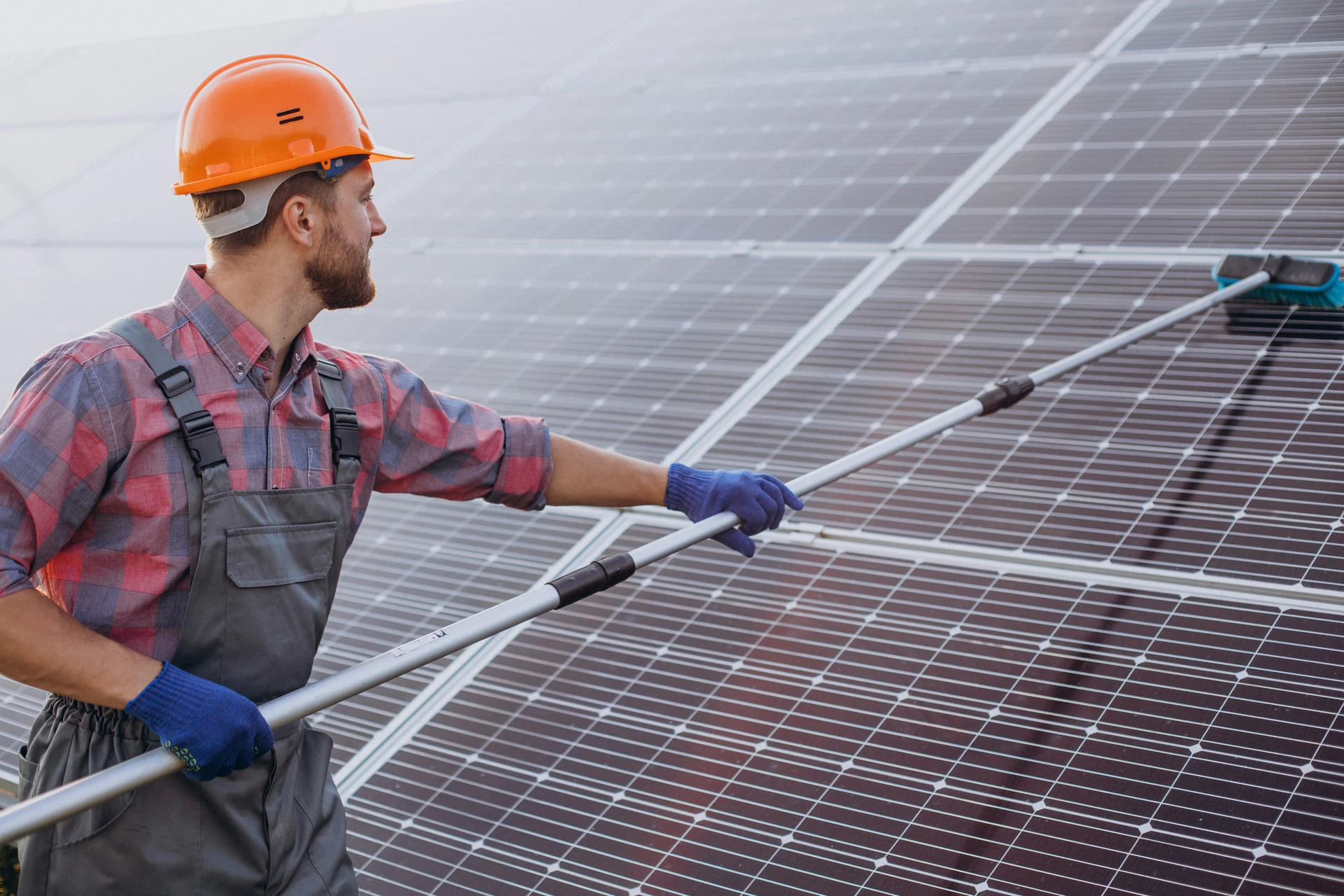Mitarbeiter mit Helm reinigt Solarmodule mit einer Teleskopbürste